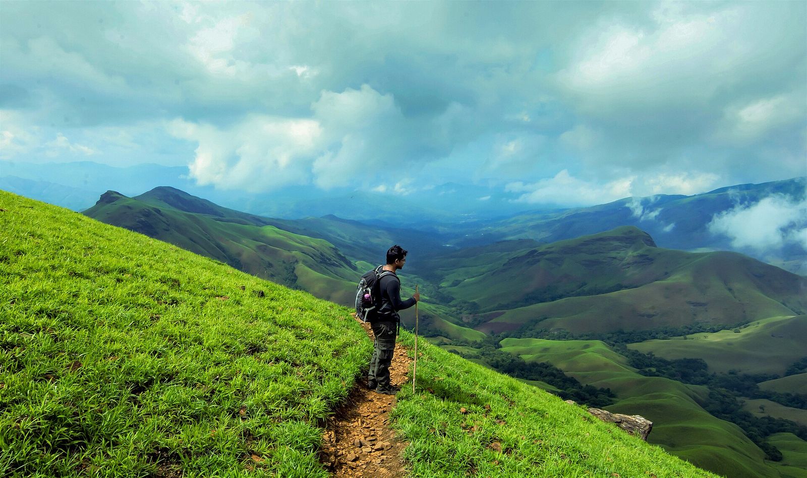 A trekker on a grassy slope looking across the green Kudremukh hills
